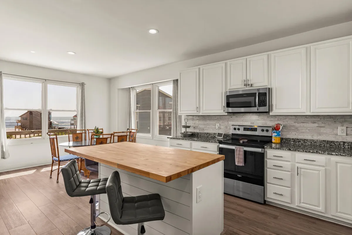 A gourmet kitchen with a central island, granite countertops, stainless steel appliances, and large picture windows that look out onto the water. The warm, welcoming atmosphere is ideal for preparing meals while enjoying the view.