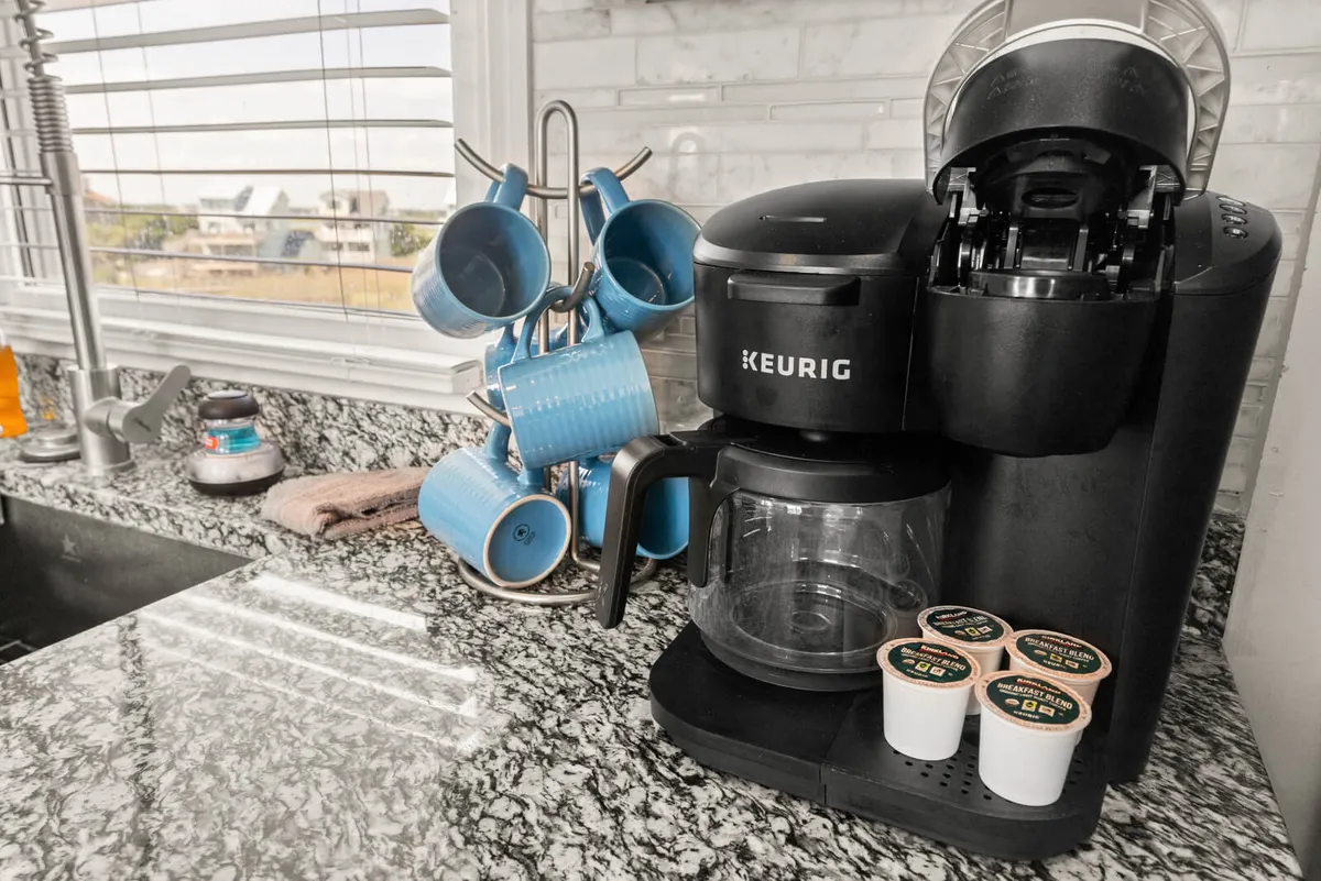 A cozy corner in the kitchen with a Keurig coffee maker, blue mugs, and a granite countertop. The space is inviting and reflects the comfort of modern amenities.