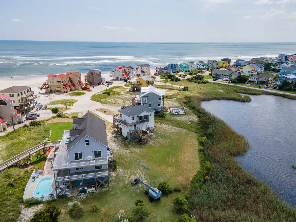 A sweeping exterior shot of beachfront properties, a sparkling swimming pool, a peaceful lake, and colorful houses. The scene suggests a vibrant, activity-filled neighborhood where guests can enjoy swimming, beachcombing, picnicking, and more—all within easy reach of the property.
