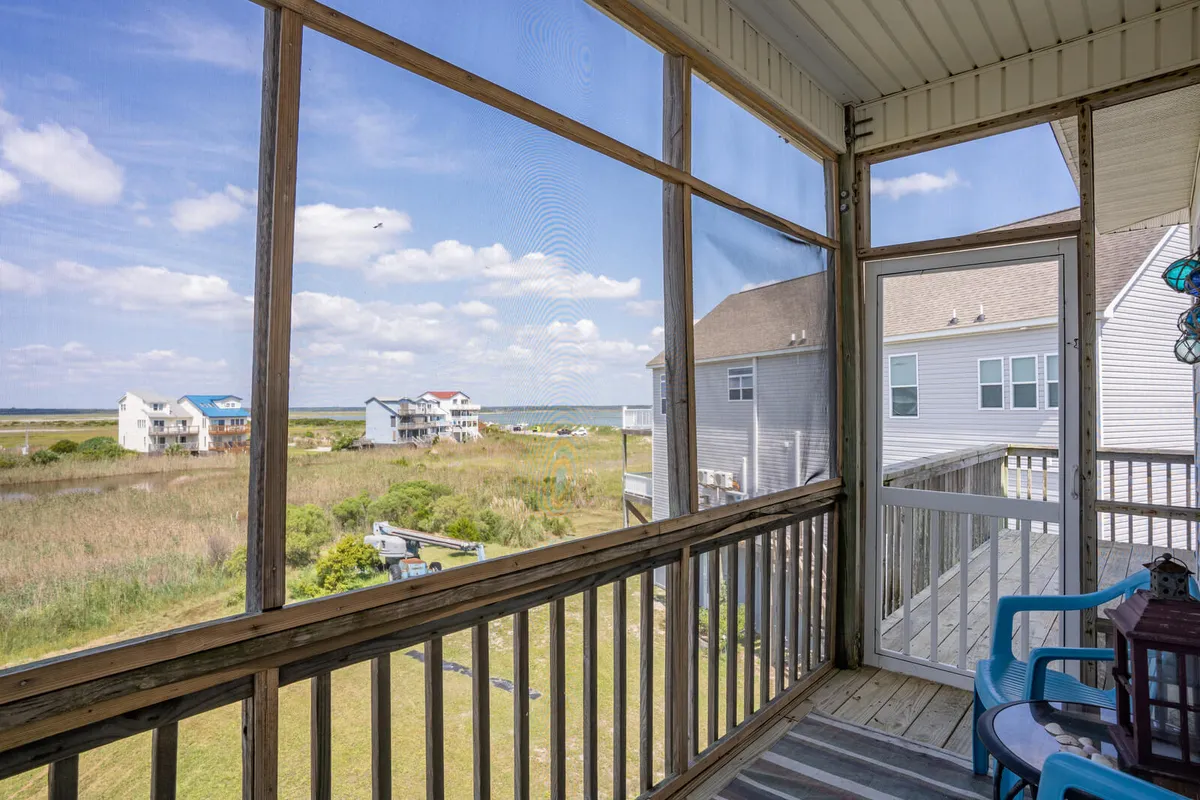 This image offers a tranquil view of a screened-in porch with blue chairs, wooden railings, and a scenic backdrop of the landscape beyond. Soft light streams through the screens, highlighting the welcoming, shaded atmosphere ideal for morning coffee or restful afternoons.