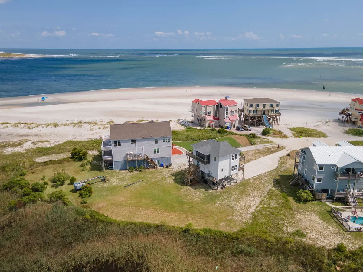 A sweeping exterior shot of beachfront properties with sandy dunes and expansive ocean views. The scene suggests easy access to the beach for fishing, boating, and water sports, with the natural beauty of the coast on full display.