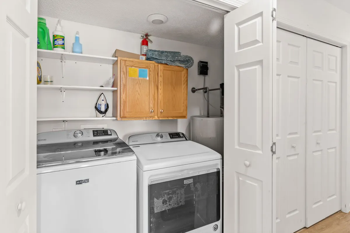A practical laundry area with washing machines, wooden cabinets, and organized shelves filled with cleaning supplies. The space is neat and thoughtfully designed for guest use.